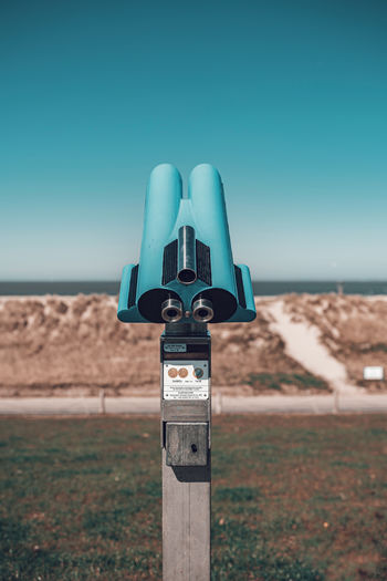 Binoculars on beach against clear blue sky