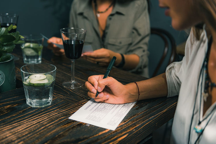 Midsection of woman writing on paper at table in restaurant