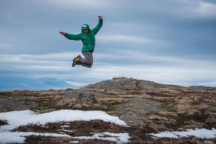 Man wearing jacket jumps off of rock in akureyri, iceland