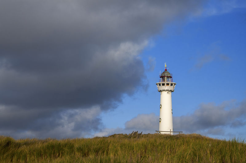 White lighthouse on the dunes near the sea under a cloudy sky