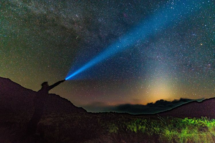 Silhouette man holding flashlight against star field at haleakala crater