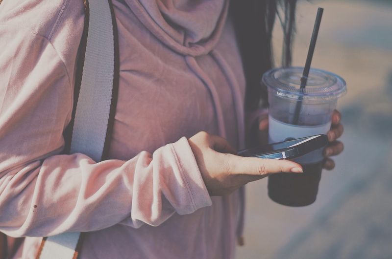 Midsection of woman using mobile phone while holding drink