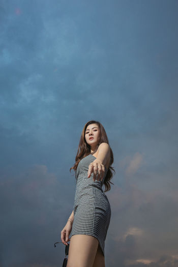 Low angle portrait of woman standing against sky