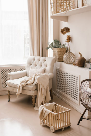 The living room is decorated in beige tones. a chair with a blanket and decor on the shelves 
