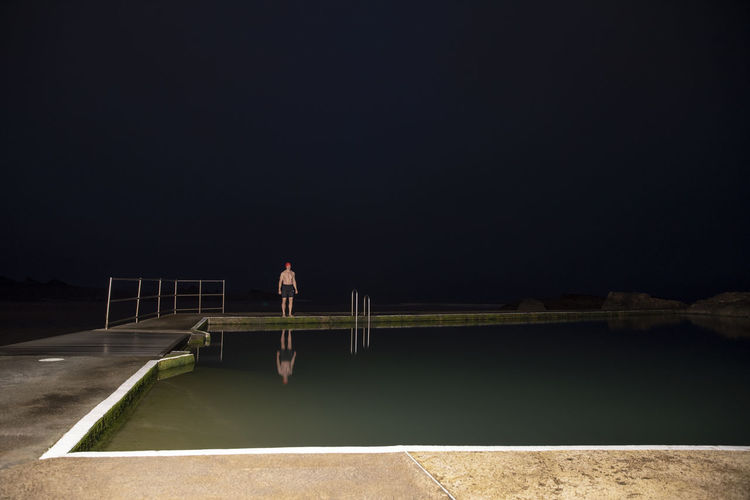 Rear view of man walking on pier against sky at night