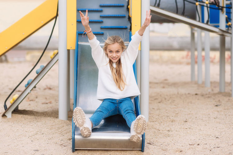 Portrait of happy girl sitting on slide at playground