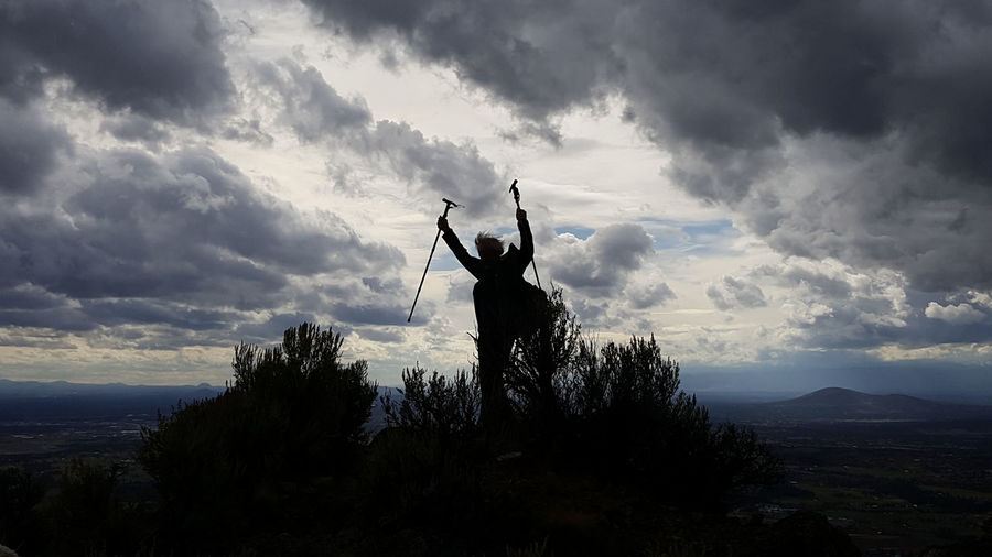 Rear view of silhouette man standing on mountain against sky