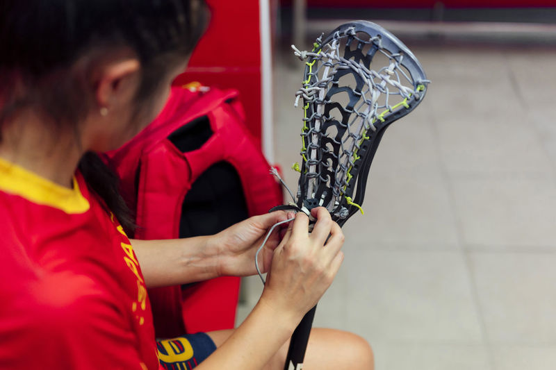 Athlete adjusting string of lacrosse stick in locker room