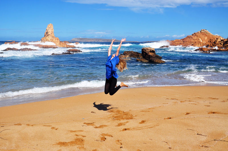 Woman jumping at beach in minorca island