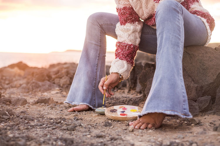 Low section of mature woman painting pebble at shore
