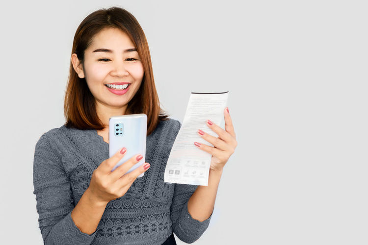 Portrait of smiling young woman holding smart phone against white background