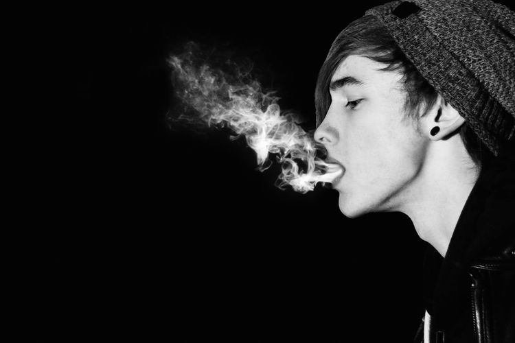 Man blowing smoke against black background