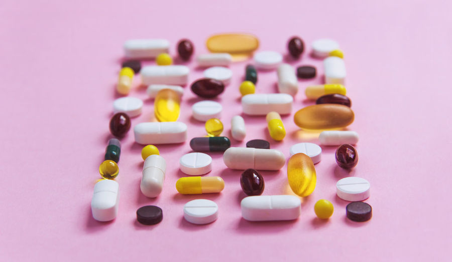 Different types of pills lie on a pink background, medicine treatment, vitamins, antibiotic