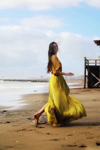 Woman with yellow dress on beach against sky