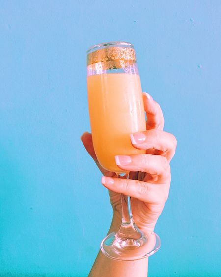 Cropped image of woman hand holding mimosa drink against clear sky