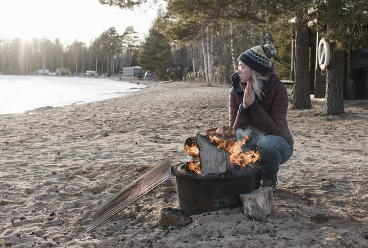 Woman warming up by a camp fire on a beach in winter in sweden