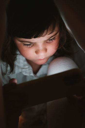 Girl under a blanket using a mobile phone at home