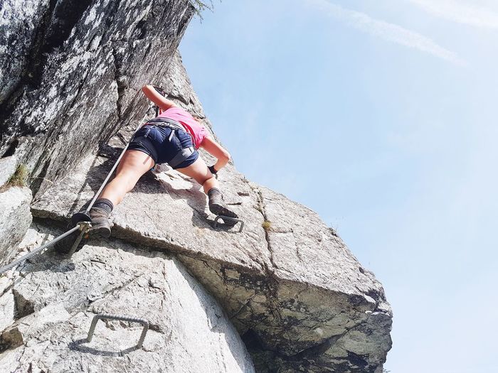Low angle view of woman climbing on rock against sky