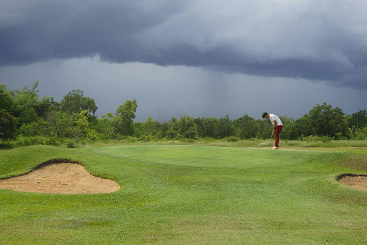 Man playing golf course against sky