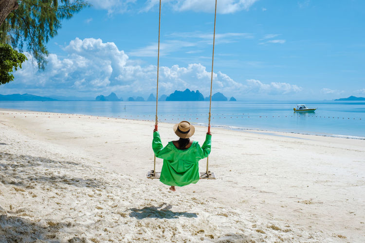 Man swinging at beach against sky