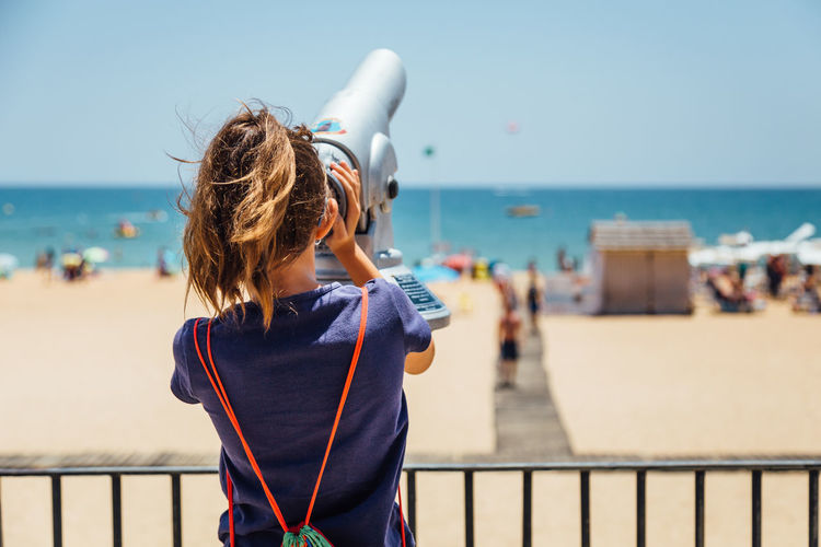 Rear view of woman looking through coin operated binoculars at beach