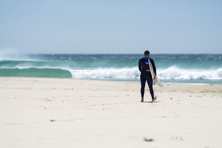 Full length of surfer man on beach against sky. 