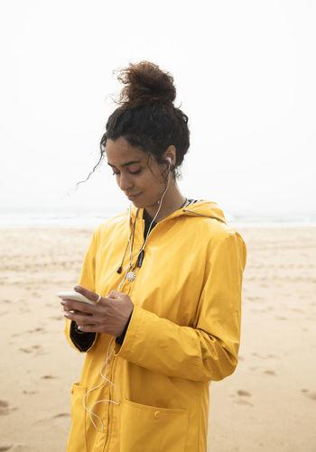 Smiling woman using mobile phone while standing at beach