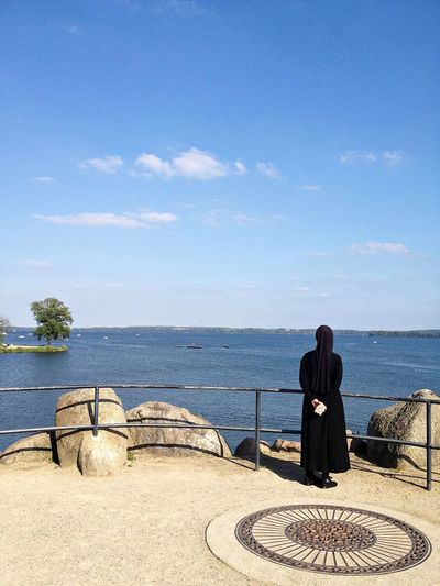 Rear view of a nun overlooking calm blue sea
