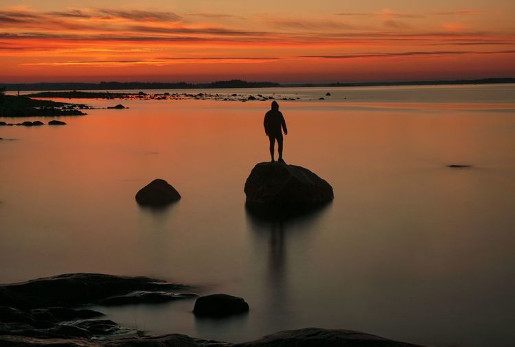 Rear view of silhouette man standing on rock at sunset