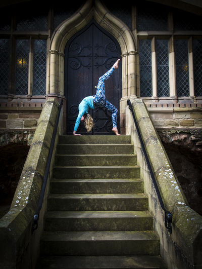 Young woman practicing yoga on staircase against church