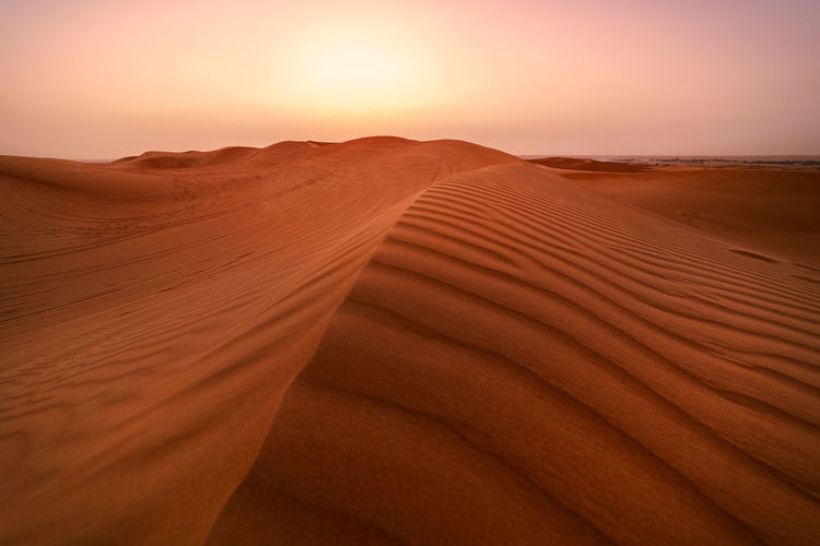 Sand dunes in desert against sky during sunset