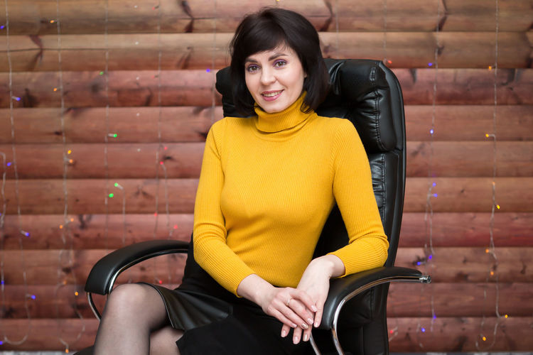 A caucasian adult woman is sitting in a leather armchair in a bright yellow jacket against