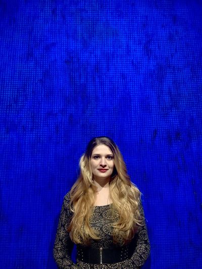 Portrait of beautiful young woman standing against blue background