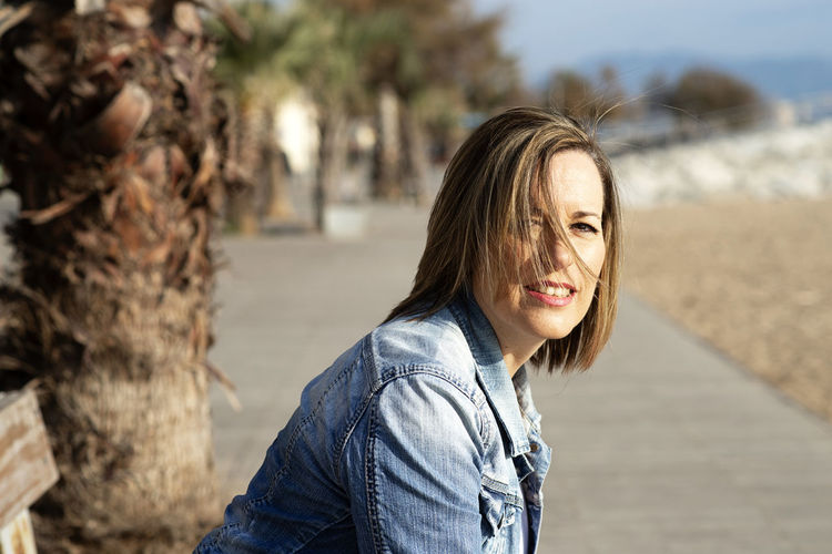 Smiling woman sitting on a bench near the beach while looking camera