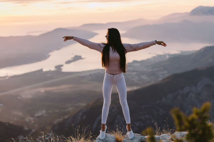 Woman with arms outstretched standing on mountain against sky