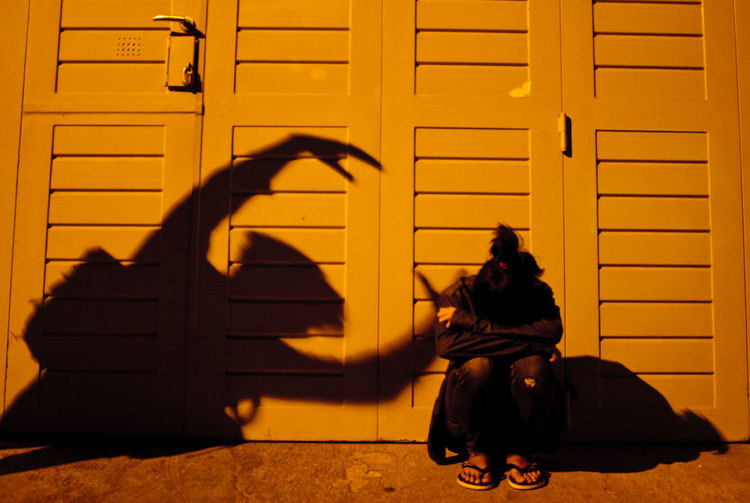 Optical illusion of shadow reaching depressed woman crouching against closed door