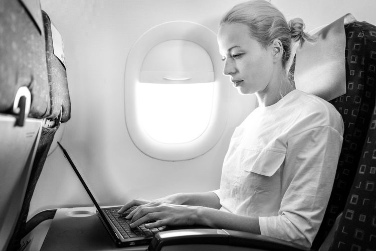 Side view of businesswoman working on laptop sitting at airplane