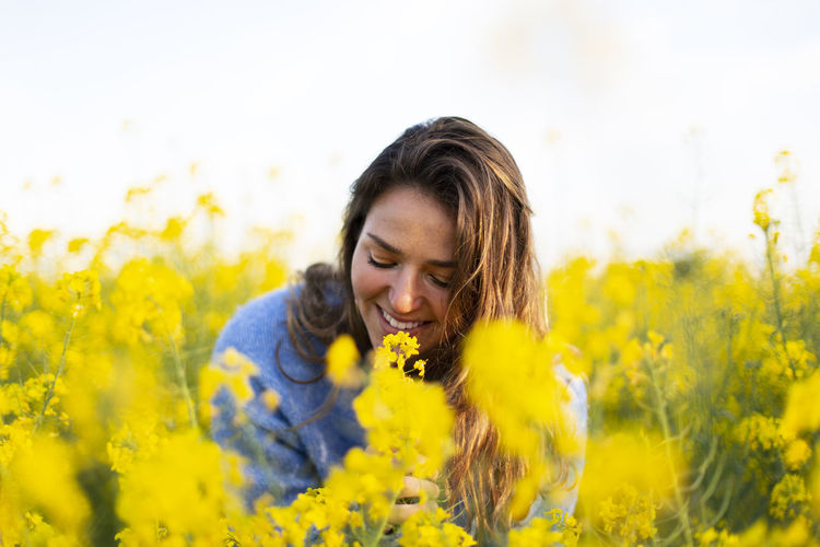 Portrait of smiling woman smelling yellow flowers on field