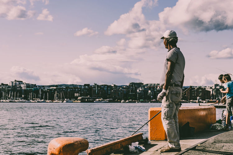 Rear view of man standing by river in city against sky