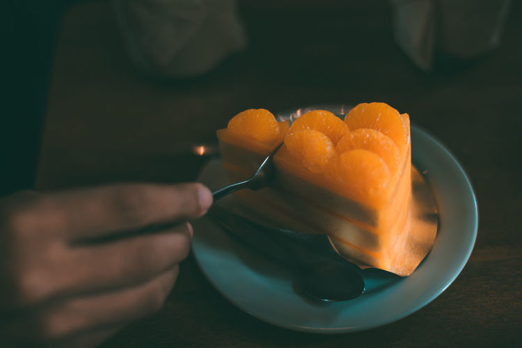 Cropped image of person eating orange cake in plate
