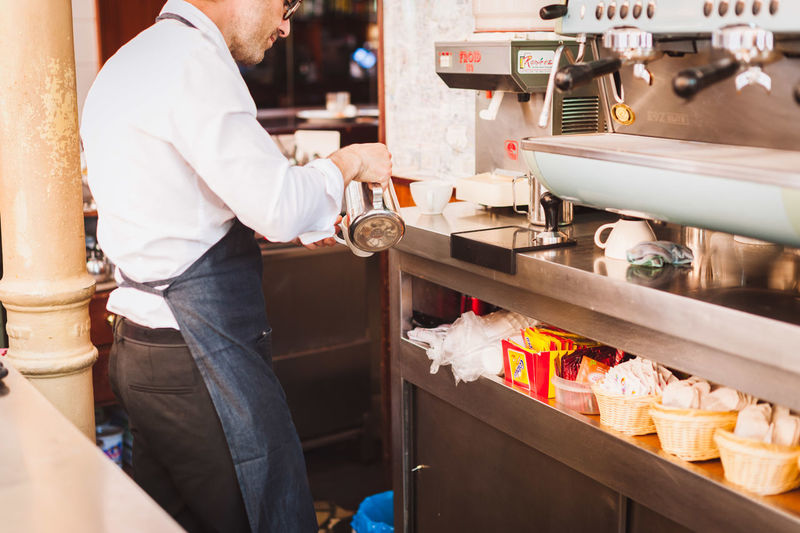 Midsection of male owner pouring coffee in cup