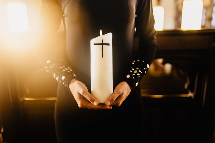 Midsection of woman holding illuminated candle at church