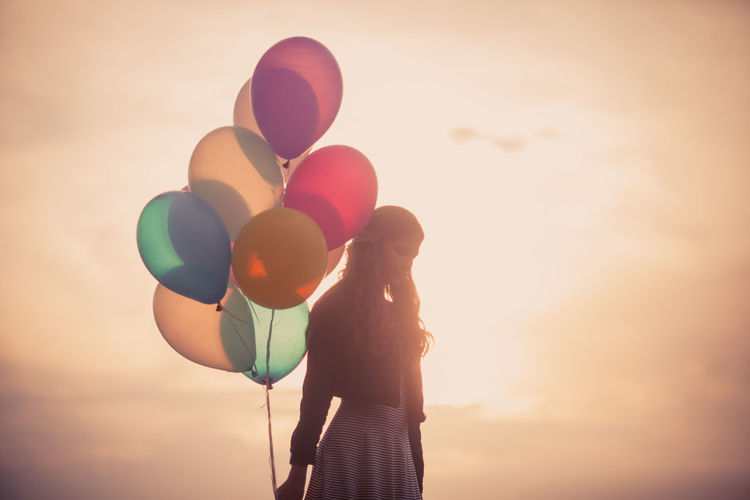 Midsection of woman holding balloons against sky during sunset