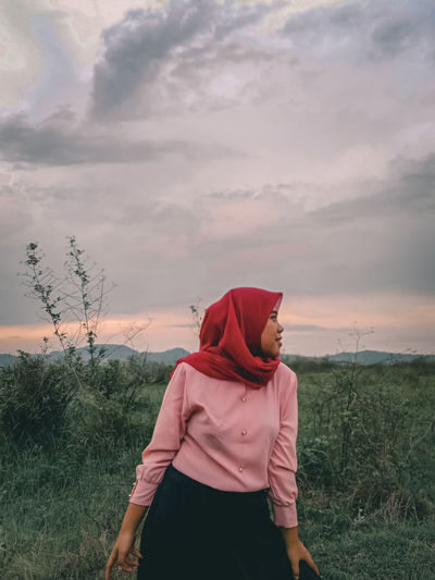 Woman wearing hijab standing on land against cloudy sky during sunset
