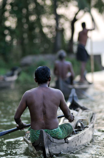 Rear view of shirtless man on boat at river