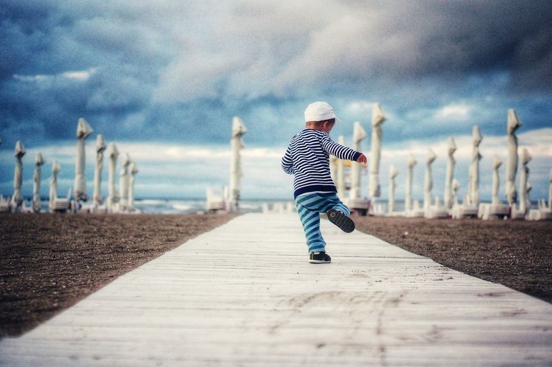 Baby boy running on the beach under dramatic sky