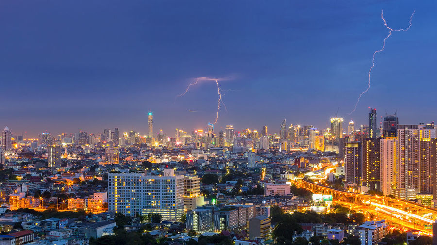 High angle view of illuminated city against lightning at dusk
