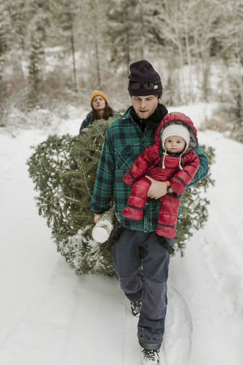 Parents with daughter pulling pine tree in forest during winter
