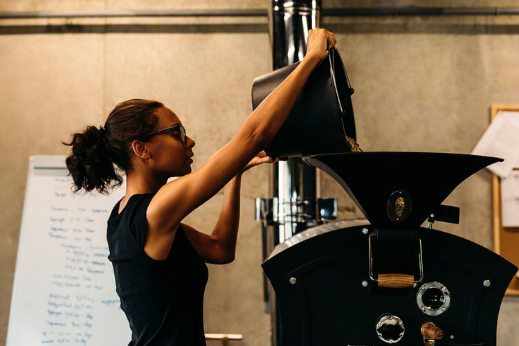 Beans Coffee One Person Only Small Business Worker Bucket Businesswoman Casual Clothing Fabric Holding Indoors One Person Operation Owner Preparing Process Professional Real People Roasting Coffee Side View Standing Technology