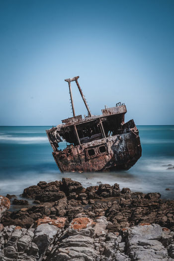 Sailboat on rocks by sea against sky